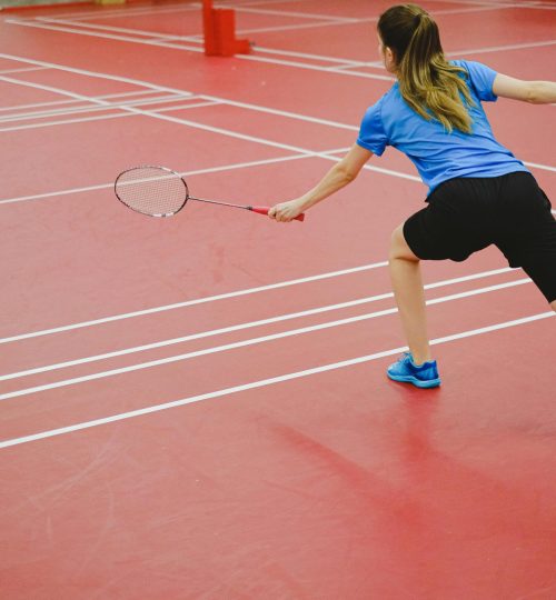 Back view of a woman playing badminton on an indoor court. Action shot capturing skill and movement.